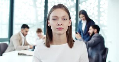 Modern şirketlerin beyaz kadın işçilerinin, modern şirketlerin ofisindeki kameraya bakan ciddi düşünceli portresi. Çekici genç bir kadın resmi kıyafetler içinde yönetici olarak çalışıyor..