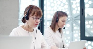 Modern çağrı merkezinde müşteri desteği temsilcisi olarak çalışan iki beyaz kadının portresi bilgisayar ve kulaklık kullanarak müşterilerle internet üzerinden konuşuyor. Çağrı merkezi kavramı.