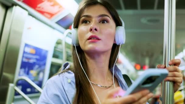 坐在电车里 戴着无线耳机 笑着迷人的女人 大城市的生活方式 地铁里的女性通过手机短信观看视频聊天 — 图库视频影像