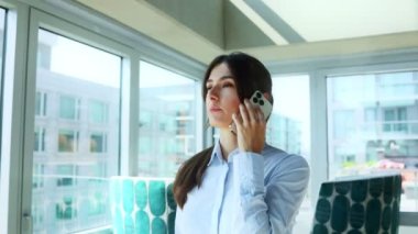 Kafkasyalı genç bir kadın, ofis çalışanı, pencerenin önünde dikilip, düşünceli bir şekilde başka tarafa bakıyor ve telefonla konuşuyor. Büyük şirket binasında cep telefonuyla arayan başarılı bir kadın..