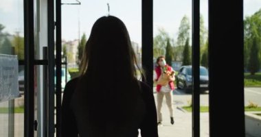 Kadın müşterinin kuryesiyle dışarıda buluşması. Koruyucu maske takan beyaz bir teslimatçı müşteriye kese kağıdı veriyor. Karantina sırasında teslimat servisi.