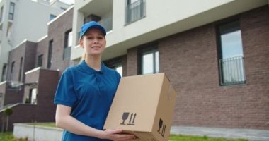 Mavi üniformalı, açık havada elinde paketle duran beyaz güzel bir kadının portresi. Güzel bayan kurye paketini veriyor ve kameraya gülümsüyor.