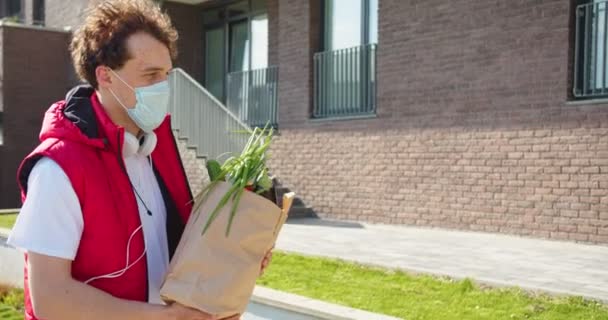 勤勤恳恳 头戴医疗面罩的高加索送货员把装有食物的纸袋送给附近的女性顾客 大流行病和保健概念 — 图库视频影像