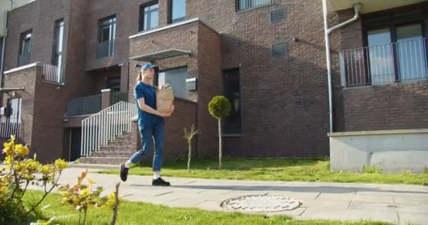 送货的女人戴着蓝色的帽子走在街上 手里拿着纸袋 检疫期间运送包裹的快递员 邮寄和网上订购概念 — 图库视频影像