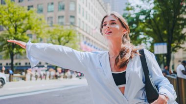 Büyüleyici bir beyaz kadın portresi büyük şehirde gülümsemeyi durdurmak için el sallıyor ve kaldırıyor. Çekici neşeli kız şık kıyafetler giyerek sokakta dikiliyor. Taksi kavramı.