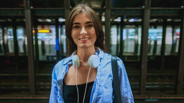 Güzel kadın işçi metroda duruyor. Meşgul ve kalabalık bir metroda duran güzel, gülümseyen kulaklıklı kız trenini beklerken kameraya bakıyor. Büyük şehir hayatı konsepti.