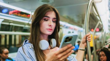 Metroda işe giderken akıllı telefondan mesaj atıp gülümseyen sevimli beyaz bir kadının portre görüntüsü. Güzel, çekici, kulaklıklı bir kız. Metro kavramı.
