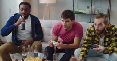 Neşeli Afro-Amerikan ve Kafkasyalı genç erkekler evlerinde video oyunları oynayıp, sohbet edip gülerler. Boş zaman konsepti. Evde eğlenen oyuncular konsolda oyun oynarlar