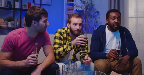 混合されたレースの肖像画 幸せな若い男性の親友は一緒にビールの飲み物と家でソファーに座って 良い会社のレジャーのコンセプトでテレビのサッカーを見ている楽しいスナックを食べて夜を過ごします — ストック動画