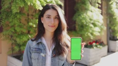 Elinde akıllı telefon tutan kadının belden yukarı portre görüntüsü ve onu sokakta dikey pozisyonda, bulanık arka planda boş yeşil ekranla gösteriyor. Telefon konseptini kullanarak