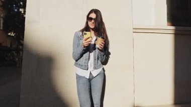 İlginç yerleri ziyaret ediyorum. Harika yerleri ziyaret ettikten ve akıllı telefonunu kullandıktan sonra yaz caddesinde elinde bir fincan kahveyle gezen şık ve mutlu bir kadın manzarası.