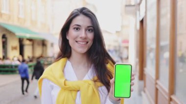 Akşamları yürürken elinde yeşil ekranlı akıllı telefon tutan esmer kadının portre görüntüsü. Teknoloji konsepti