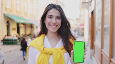Akşamları yürürken elinde yeşil ekranlı akıllı telefon tutan esmer kadının portre görüntüsü. Teknoloji konsepti