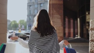 Alışverişe bayılırım. Arkasında şehir olan renkli alışveriş torbalarıyla yürürken sevimli bir kadın dans ediyor ve gülümsüyor. Yaz alışverişi. Hediyeler ve büyük satış konsepti almak.