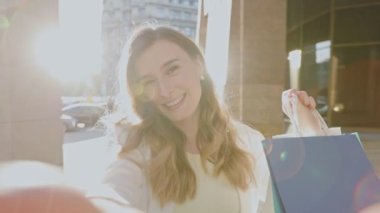 Alışveriş günü. Beyaz kadının alışveriş yaptıktan sonra mutlu olduğu selfie kamerası görüntüsü. Kız kameraya bir şeyler söylüyor ve bir sürü alışveriş paketi gösteriyor.
