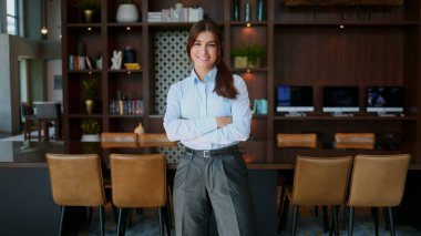 Şirketimizin zarif bayan patronunun portresi gülümseyen kameraya bakıyor. Takım elbiseli güzel bir bayan kollarını kavuşturarak ofiste duruyor. CEO kavramı.