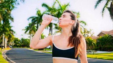 Yaz antrenmanından sonra su içen güzel bir kadın portresi. Palmiye ağaçlarının arasında koşan güzel bir kız. Spor koşusu konsepti.