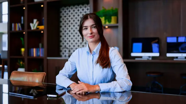 Portrait of attractive professional young woman working at company sitting at table looking at camera smiling. Beautiful successful businesswoman employer. CEO concept.