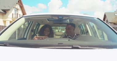 Genç ve çekici bir çift arabada oturuyor. Elinde akıllı telefon olan kız navigatör uygulaması kullanarak erkek arkadaşına yol gösteriyor. Varış yeri. Açık havada. Ön görünüm.