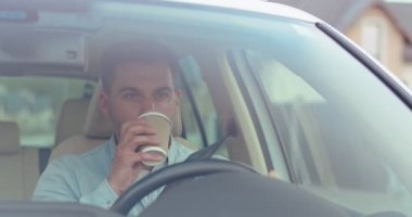 Mutlu, genç, beyaz bir adam yolda araba sürüyor etrafa bakıyor, gülümsüyor. Mutluyum, müzik dinliyorum, çay ya da kahve içiyorum. Keyfin yerinde. Afiyet olsun. Arabaların içi. Ön görünüm.