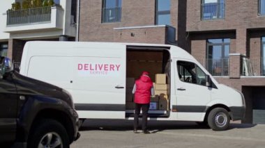 Afro-Amerikalı teslimatçı. Paket kutusunu alıcıya götürüyor. Kurye minibüsün yan kapısını kapatır ve online siparişleri teslim etmek için yola koyulur..