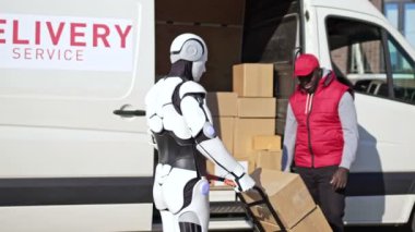 Robot bir yük arabasında paket kutuları getiriyor ve Afro-Amerikan kurye onları bir minibüse koyuyor. Kurye alıcıya paket kutusunu teslim ediyor.