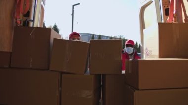 Afrika kökenli Amerikalı ve beyaz maskeli kuryeler karavandan tramvaya paket kutuları taşıyorlar. Bir müşteriye posta paketi teslimatı için yük arabasıyla gelen teslimatçılar..