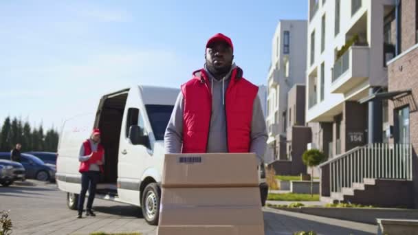 アフリカ系アメリカ人の配達人 バンからトロリーの小包箱を彫った クライアントに郵便小包を配達する方法に関する宅配便 — ストック動画