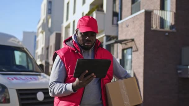 Африканський Американський Чоловік Доставки Обробляє Коробку Посилок Прогулюючись Вулиці Планшетом — стокове відео
