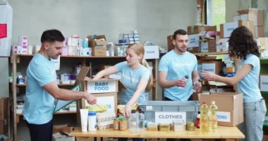 Mavi üniformalı bir grup beyaz gönüllü panoya not alıyor ve depodaki bağış kutularını paketliyor. Boş zamanlarında hayır kurumunda çalışan gençler.