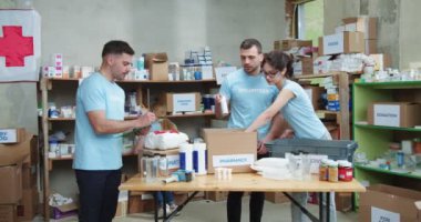 Erkek sosyal hizmet görevlisi, Kızıl Haç Yardım Fonu 'nda karton kutular dolusu ilaç paketlerken not alıyor. İnsani yardım kavramı.