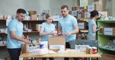 İnsani yardım projesinde çalışırken ihtiyacı olan insanlar için ilaç paketleyen beyaz bir grup. Mavi tişörtlü, İskoç mukavva bağış kutularıyla takılan beyaz adam..