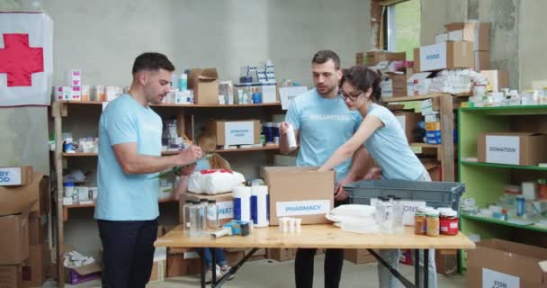 Férfi Szociális Munkás Jegyzetel Írótáblán Miközben Önkéntesekből Álló Csapat Kartondobozokat — Stock videók