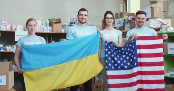 一组参加义工的食品银行工作人员一边站在慈善基金会的仓库里 一边拿着乌克兰和美国国旗 准备在乌克兰提供人道主义援助的美国志愿人员 — 图库视频影像