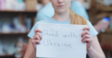 Ukrayna 'da yemek bankasında beklerken mavi tişörtlü bayrağı Ukrayna' nın yanında gösteren genç gönüllü bayanı yakından çek. Savaş sırasında insan kavramı, bağış ve destek.