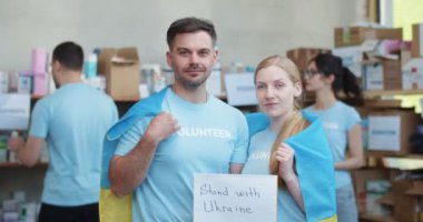 Kafkasyalı gülen adam ve kadın gönüllü olarak Ukrayna 'nın yanında afiş taşıyarak yardım kuruluşunda poz veriyor. İnsani yardım, destek ve savaş karşıtı konsept.