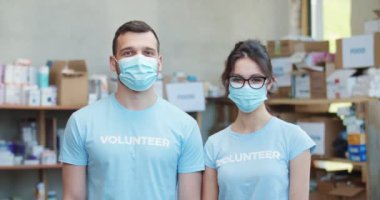 Genç erkek ve kadın gönüllüler yardım fonu deposunda poz verirken tıbbi koruyucu maskeler takıyorlar. Pozitif beyaz insanlar boş zamanlarını muhtaç insanlara yardım etmek için harcıyorlar..