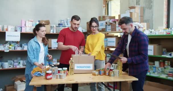 Ομάδα Εθελοντών Που Συσκευάζουν Τρόφιμα Και Ποτά Χαρτόκουτα Ενώ Στέκονται — Αρχείο Βίντεο