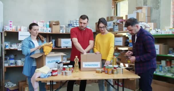 Group Young Volunteers Packing Food Clothes Boxes While Bearded Man — Stock Video