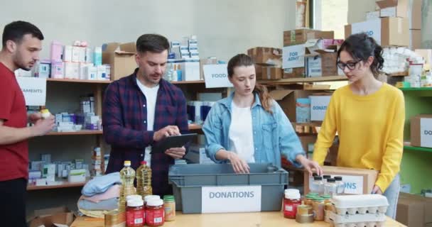 Jonge Mannelijke Vrouwelijke Vrijwilligers Liefdadigheidsfonds Verpakken Blikken Voedsel Noodzakelijke Medicijnen — Stockvideo