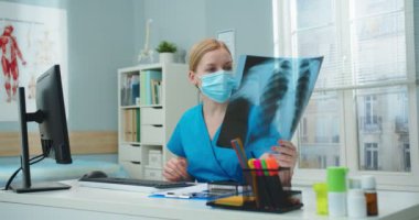 Maskeli yakışıklı beyaz hastane çalışanı masada oturup akciğerin röntgen taramasına bakıyor. Genç bayan hemşire klinikteki bilgisayardan veri girişi yapıyor. Tıp, sağlık konsepti.