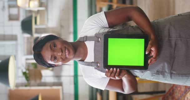 幸せな若いかなりアフリカ系アメリカ人女性労働者の垂直ビデオのエプロンに立ってカフェで仕事 カメラと笑顔を見て 緑の画面でタブレットを保持 ビジネスコンセプト 肖像画 — ストック動画