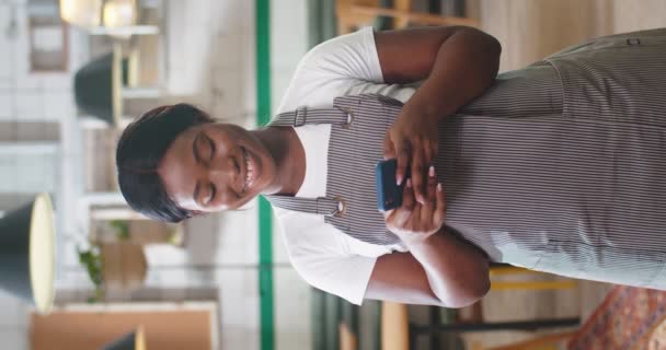 アフリカ系アメリカ人の若い若い陽気でかわいい女性の従業員の肖像画は カフェテリアに立って笑顔でスマートフォンにテキストを送ります 携帯電話でオンライン閲覧レストランでエプロンの美しい女性 — ストック動画