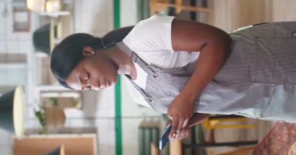 幸せなアフリカ系アメリカ人の若い美しい女性労働者の肖像画は コーヒーハウスに立って笑顔でカメラを見ているスマートフォンにテキストを送ります レストランでの作業 携帯電話で閲覧 垂直ビデオ — ストック動画