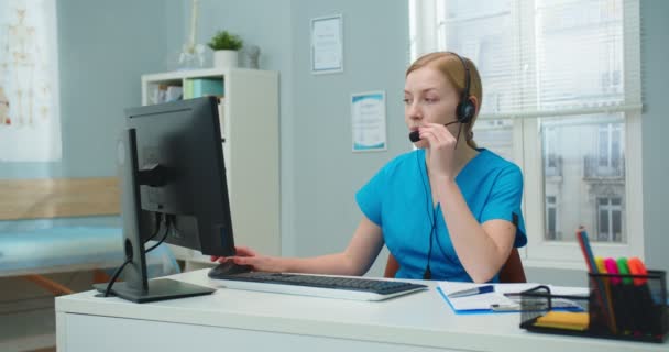 迷人的白种人女性穿着军服在医院办公室工作 在隔离期间 年轻的女护士在耳机会议上与病人交谈 医学概念 — 图库视频影像