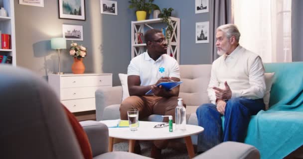 Белый Пожилой Пациент Мужчина Разговаривает Молодым Красивым Афроамериканским Врачом Медсестрой — стоковое видео