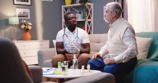 保健工作者非洲裔美国专业护士或医生在家访时与坐在沙发上的白人老年男性病人交谈 健康检查 护理工作 医疗咨询概念 — 图库视频影像