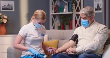 Sağlık maskeli, beyaz kadın doktor portresi. Ev ziyareti sırasında Coronavirus karantinası sırasında yaşlı bir adamın kan basıncını ölçen sağlık kontrolü.
