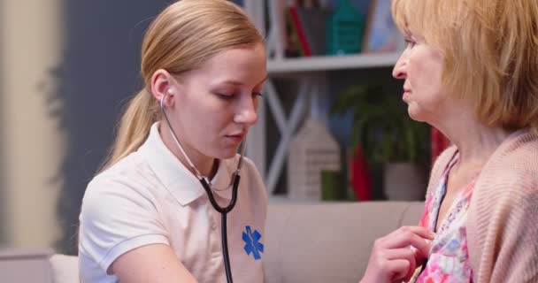 年轻漂亮的白种人专业女保健工作者护士在家访 检查时使用听诊器对老年妇女病人进行体格检查 观察其呼吸情况 — 图库视频影像