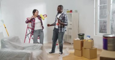 Genç ve neşeli bir çift, Afrikalı Amerikalı koca ve Asyalı eş, yeni dairenin yenilenmesi sırasında ellerinde elektrikli matkap ve boya fırçası, eğleniyorlar ve şarkı söylüyorlar, yenileme konsepti
